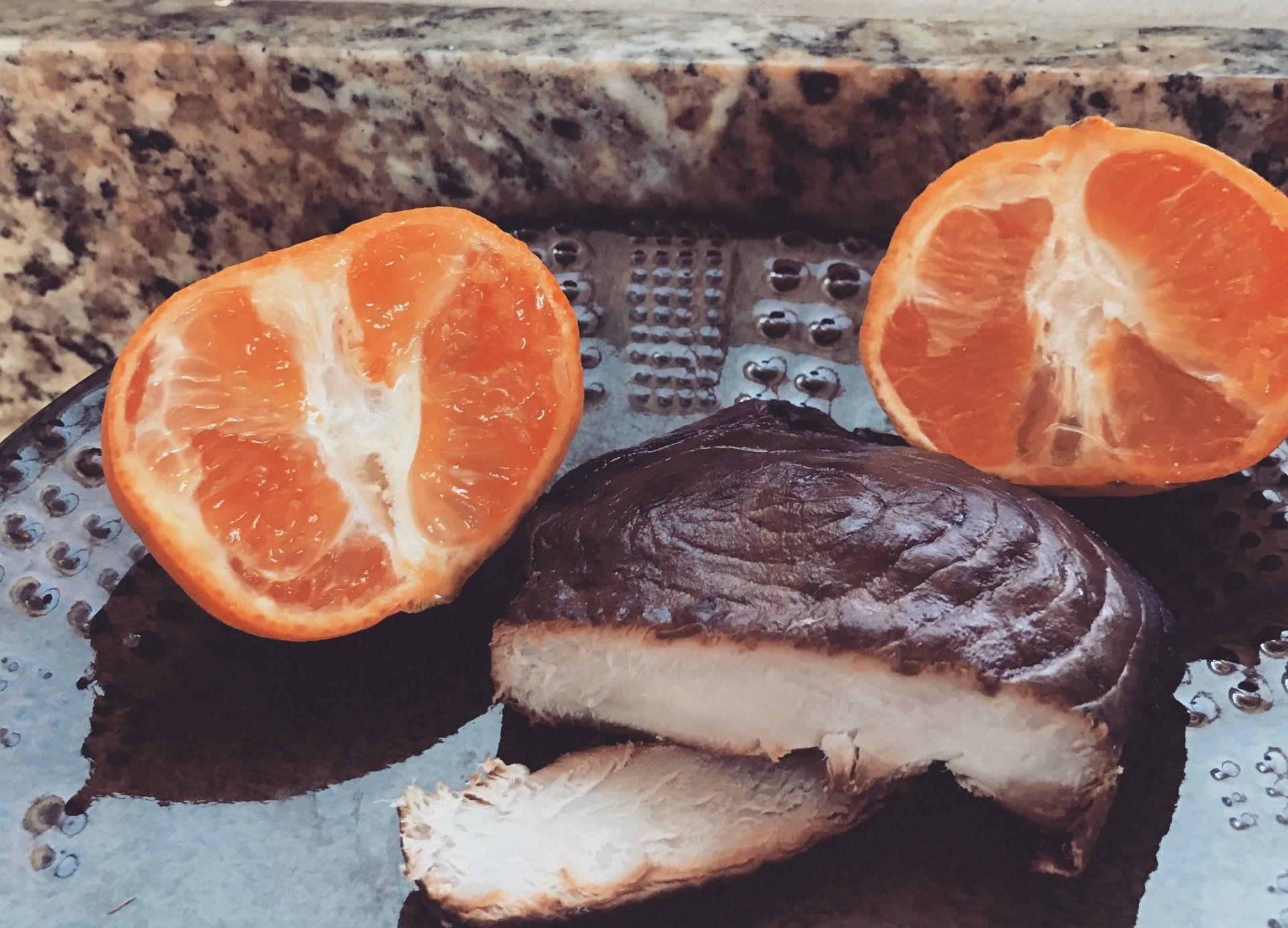 Tangerine halves and a piece of cooked meat on a black plate. Orange and brown hues.