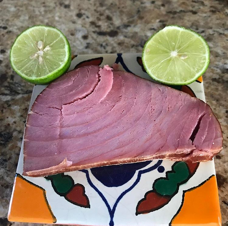 Pink tuna steak with lime halves on a decorated square tile.