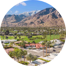 An aerial view of a residential area with palm trees and mountains in the background.