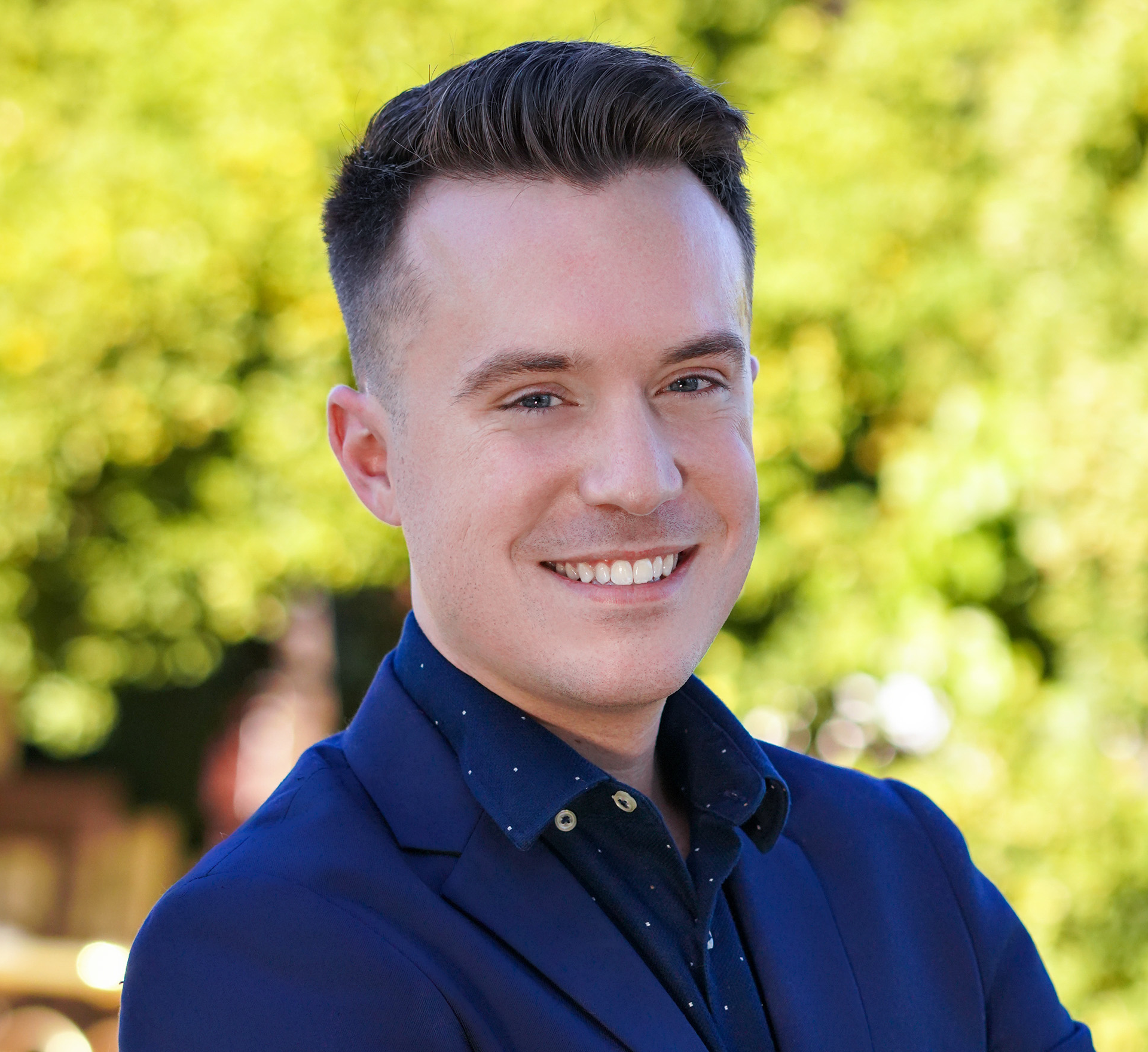 A man in a blue suit and polka dot shirt is smiling for the camera.