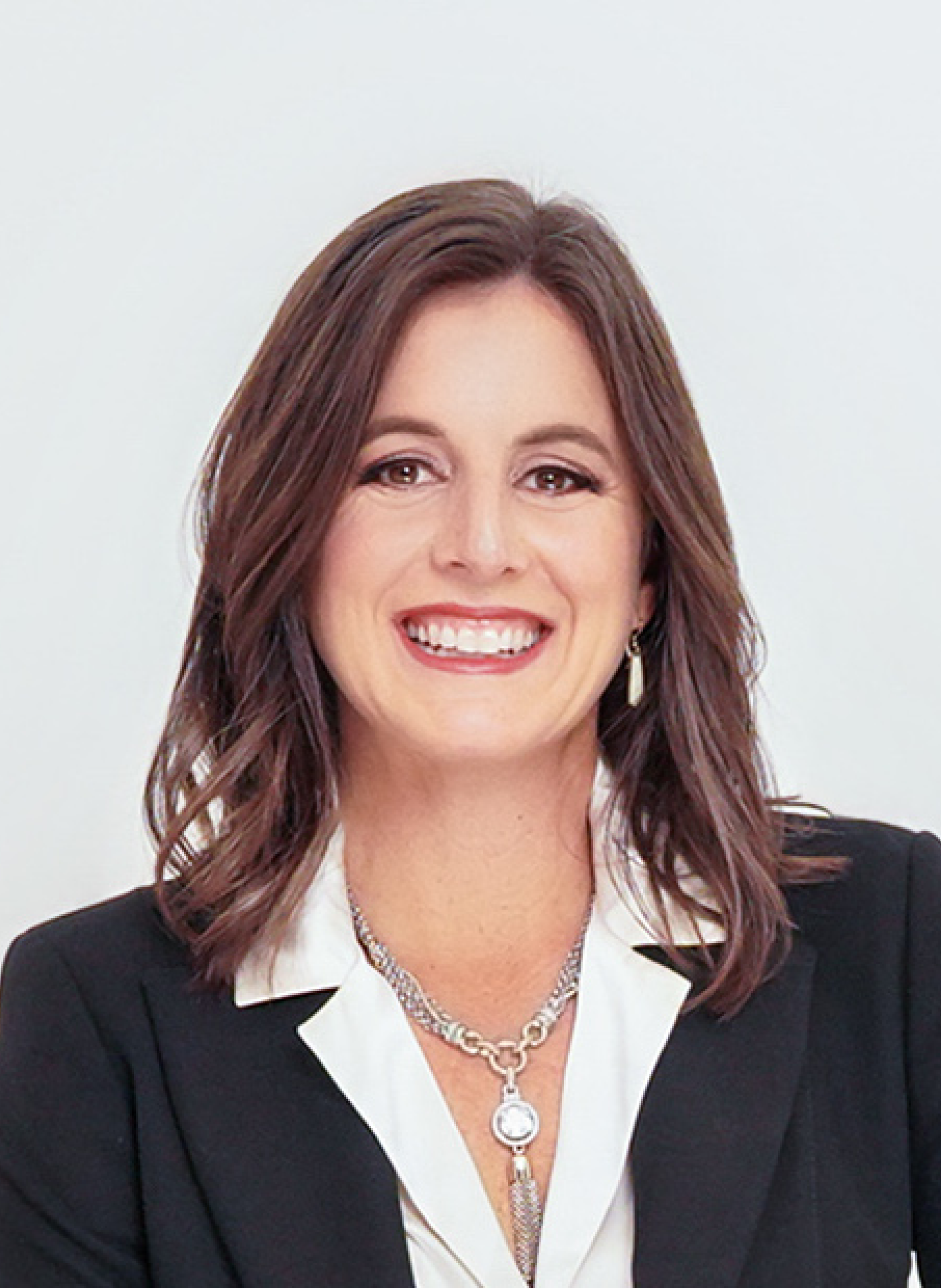 A woman in a suit and necklace is smiling for the camera.