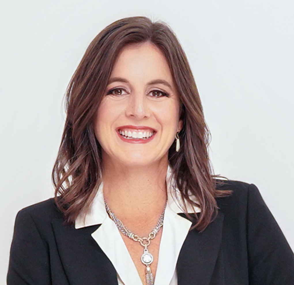 A woman wearing a black jacket and a necklace is smiling.