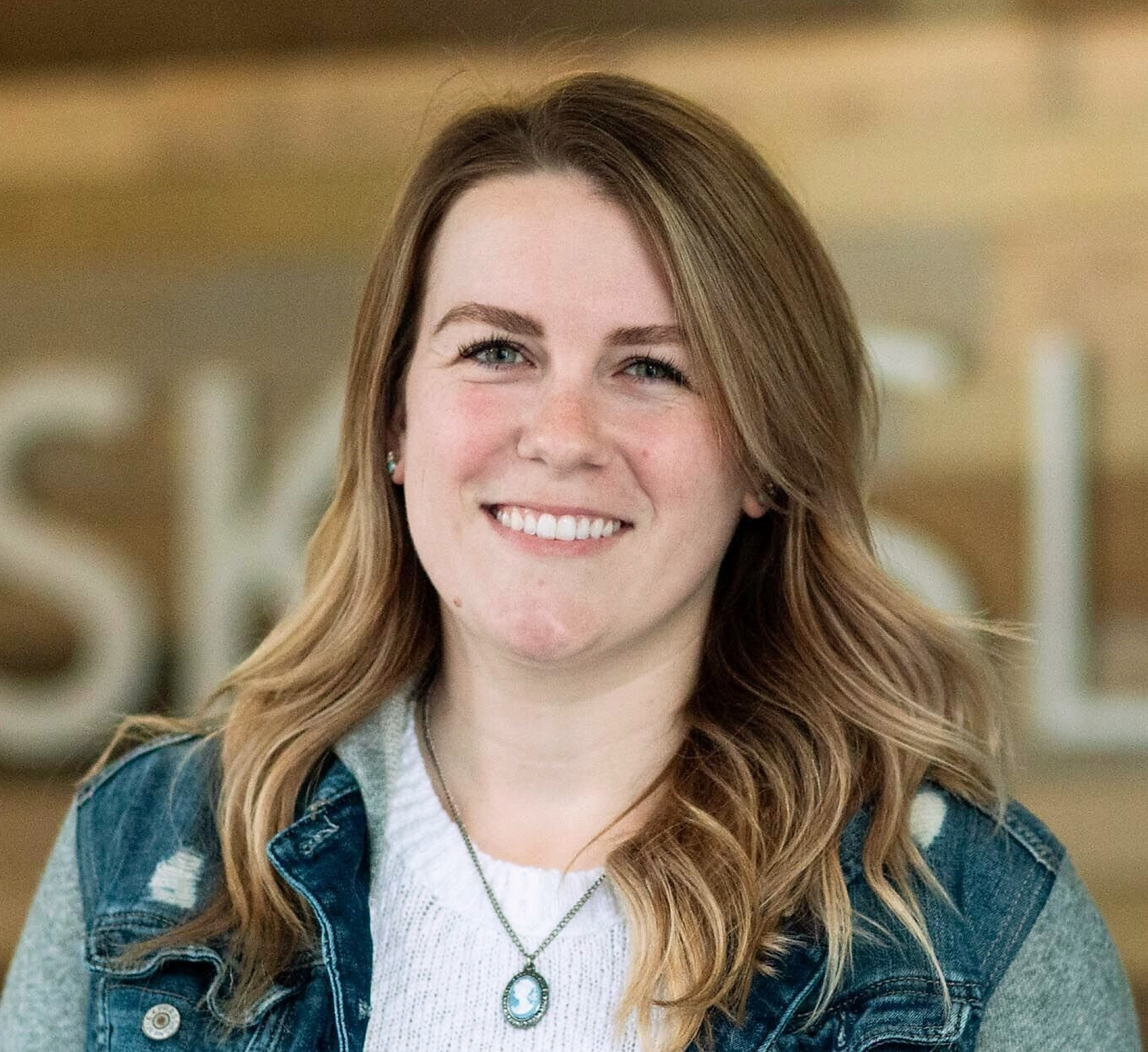 A woman wearing a denim jacket and a necklace is smiling for the camera.