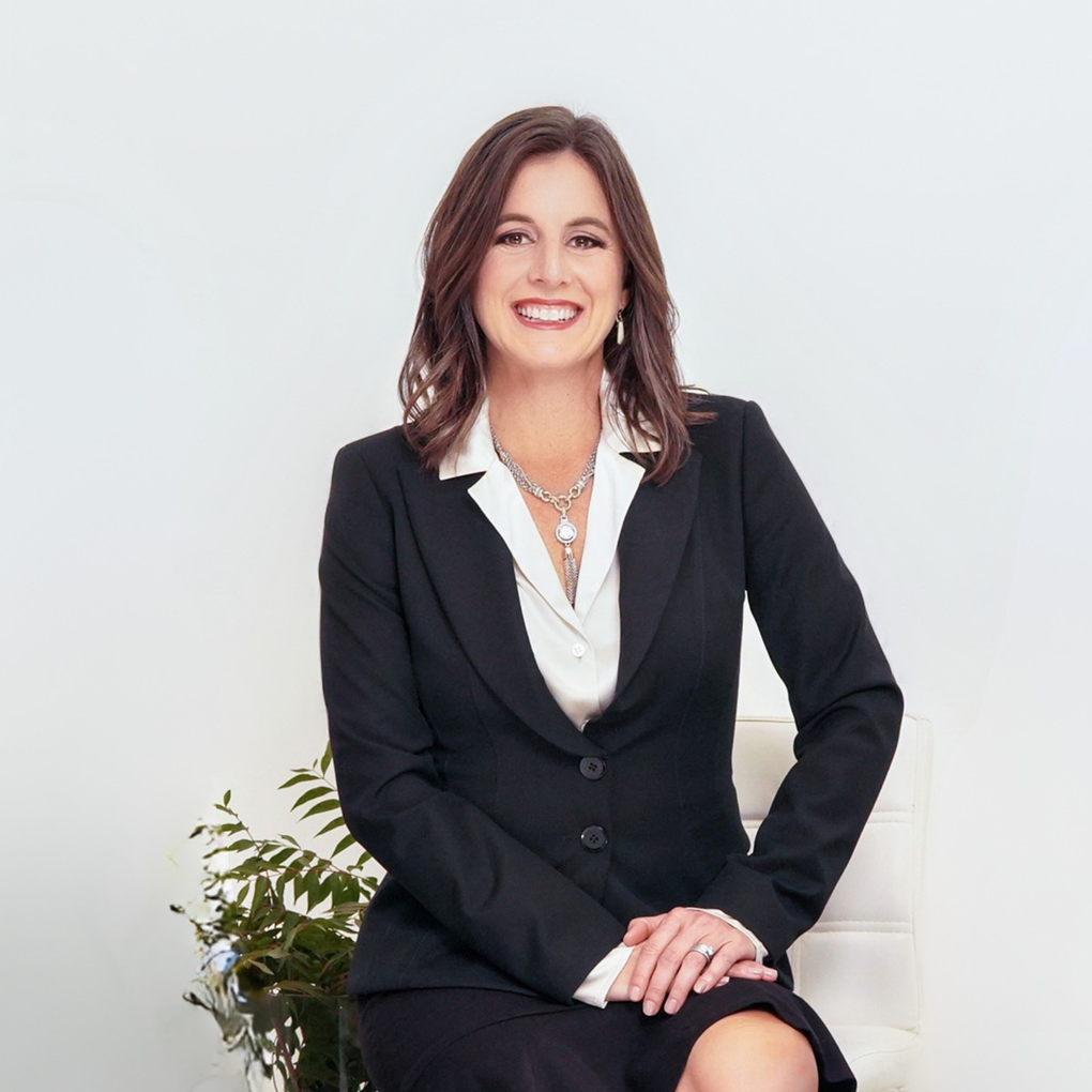 A woman wearing a black jacket and a necklace is smiling.