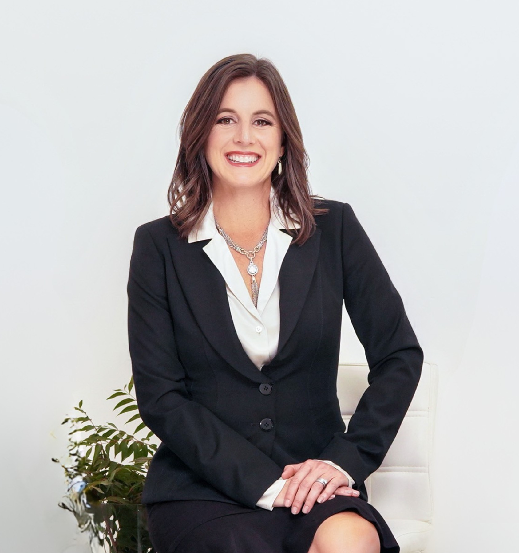 A woman in a suit and necklace is smiling for the camera.