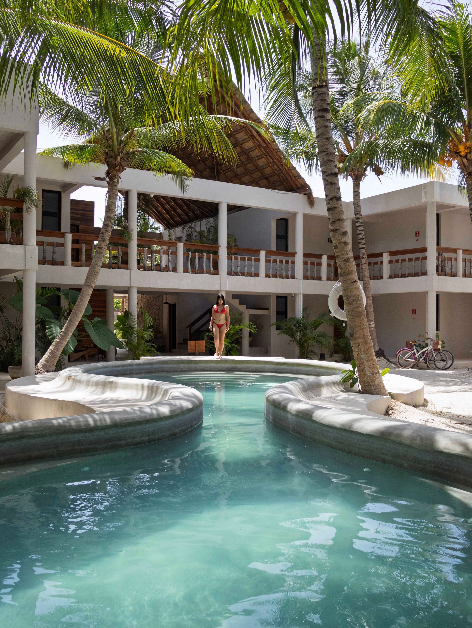Piscina del complejo con palmeras y balcones blancos alrededor de una fuente de agua turquesa que simula una laguna.