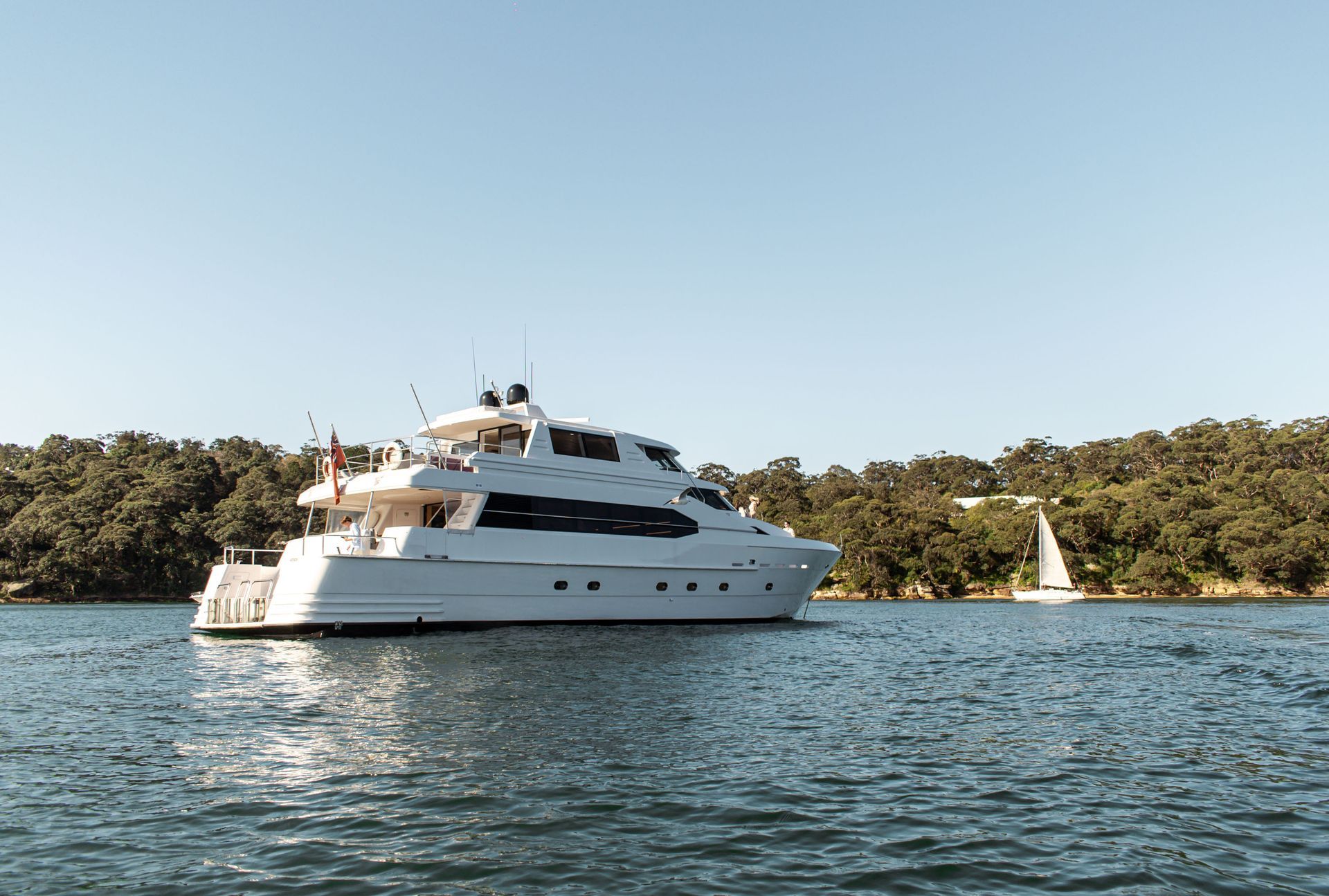 Large white yacht on calm water, people on deck, sunny day.