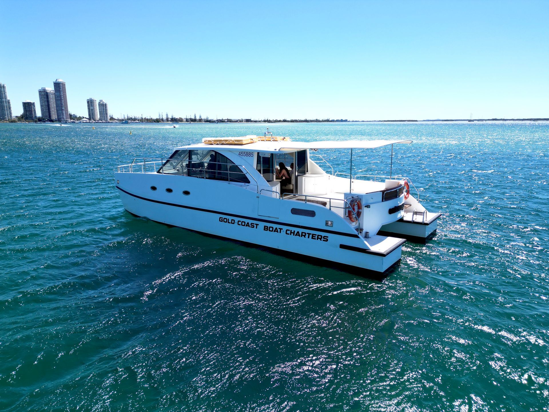 White catamaran boat on blue water with city skyline in the background.