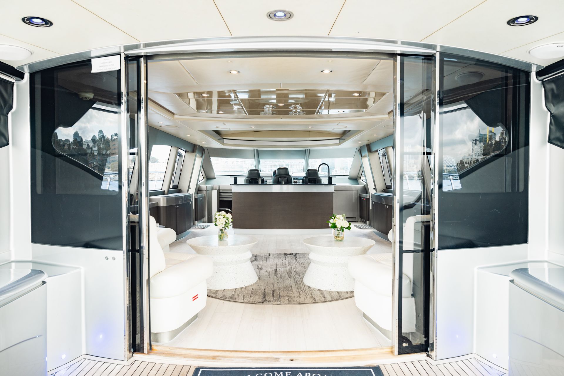 Interior of a luxury yacht. White furniture, grey rug, control panel, large glass doors.