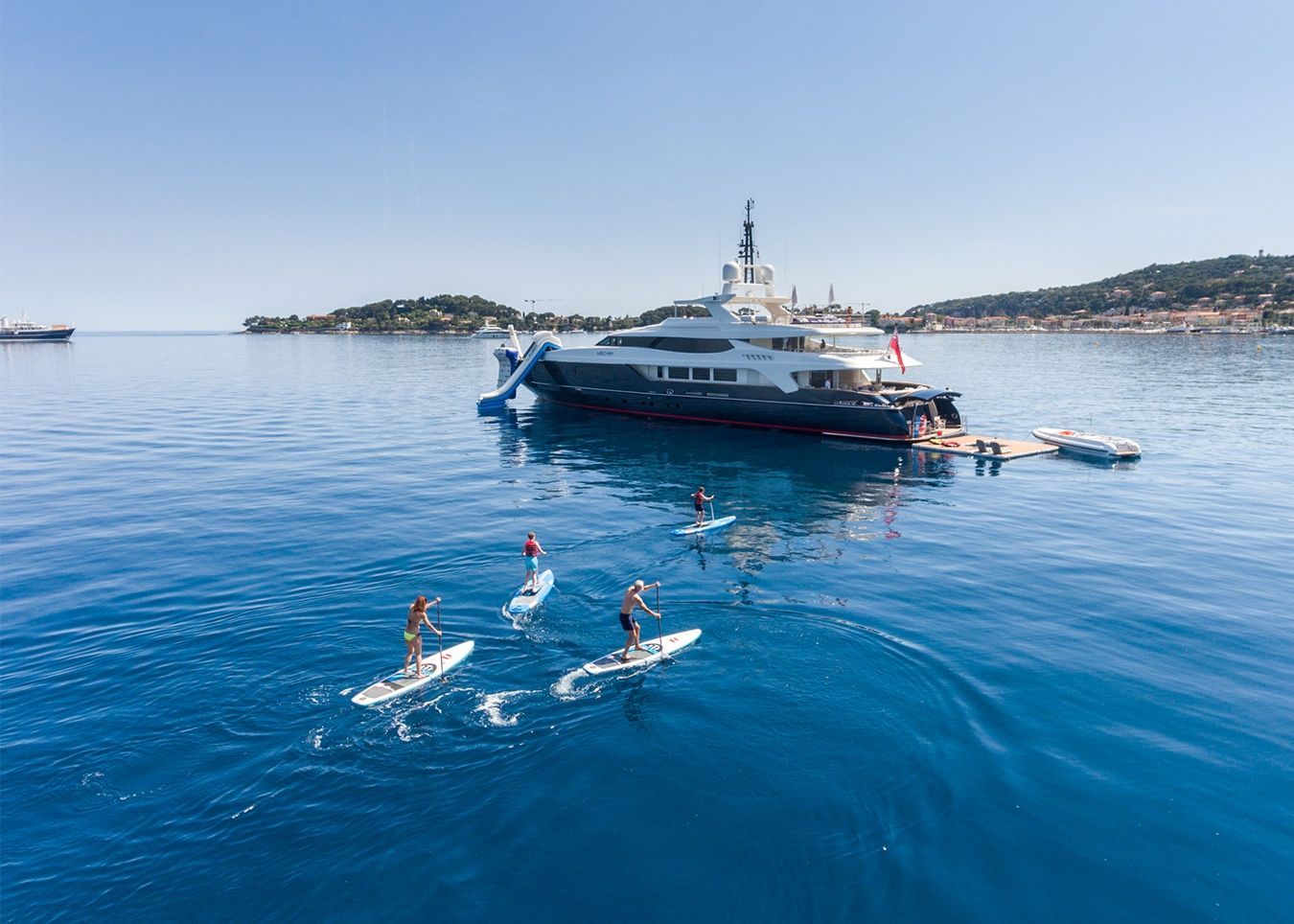 A Group of People Are Riding Paddle Boards in The Ocean in Front of A Large Yacht — Club Nautical in Gold Coast, QLD