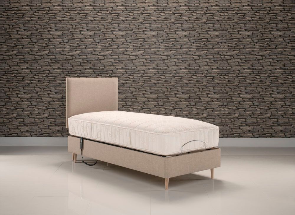 A single bed with a mattress on it in front of a brick wall.