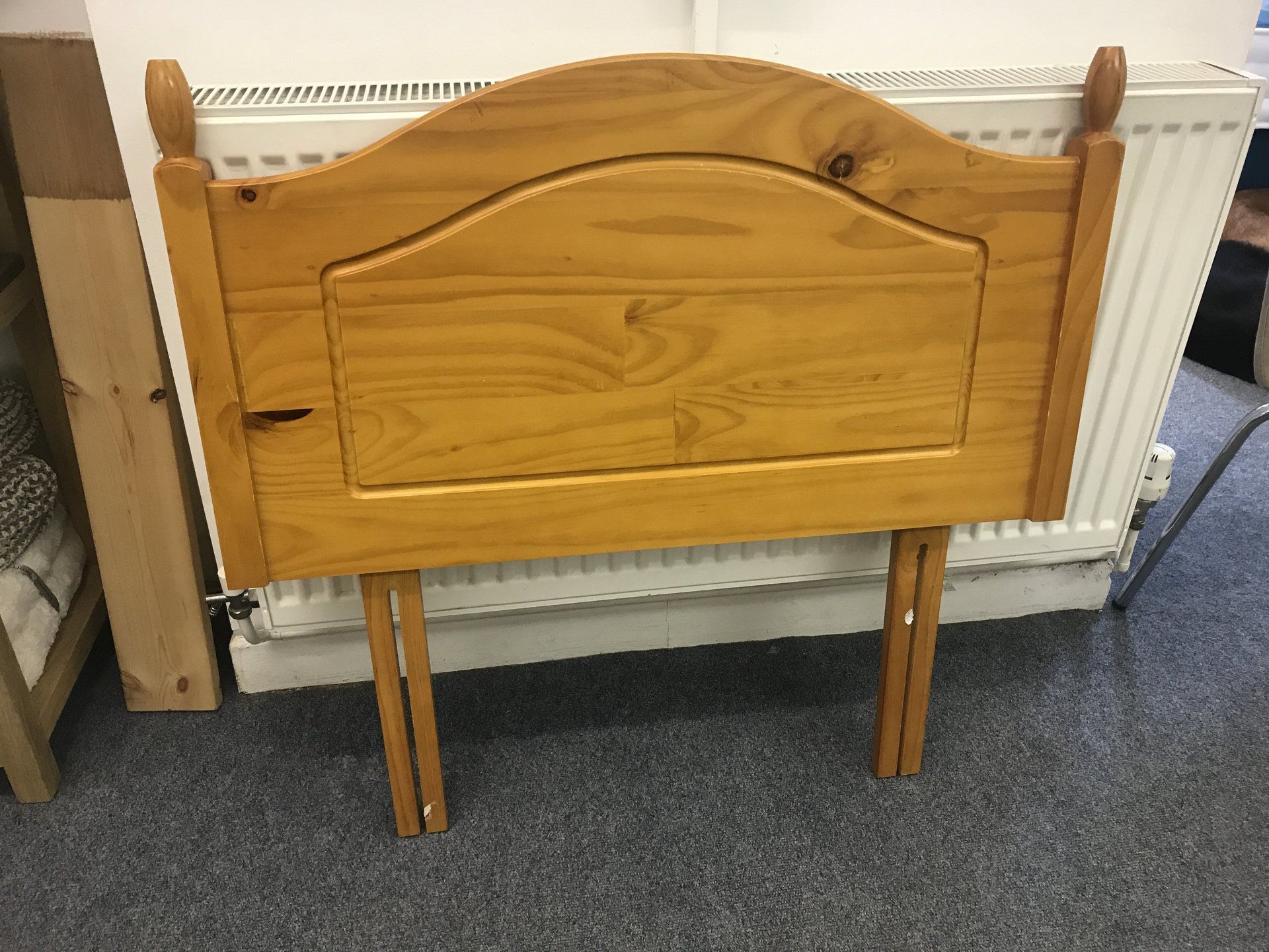 A wooden headboard is sitting on a carpet next to a radiator.