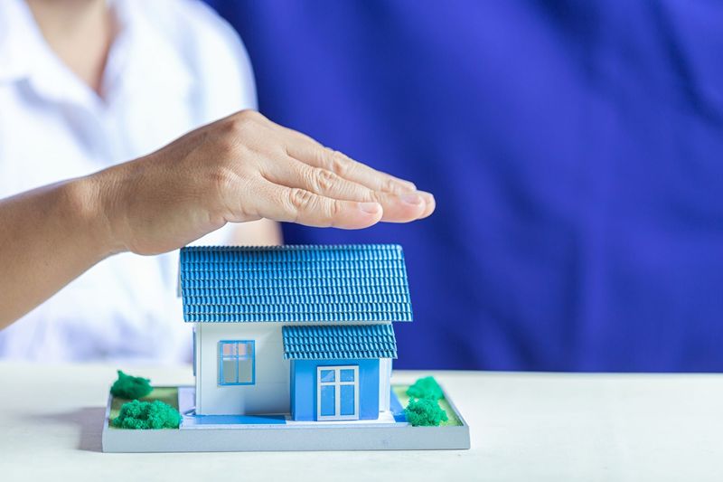 Hand hovering over a blue model house on a white table