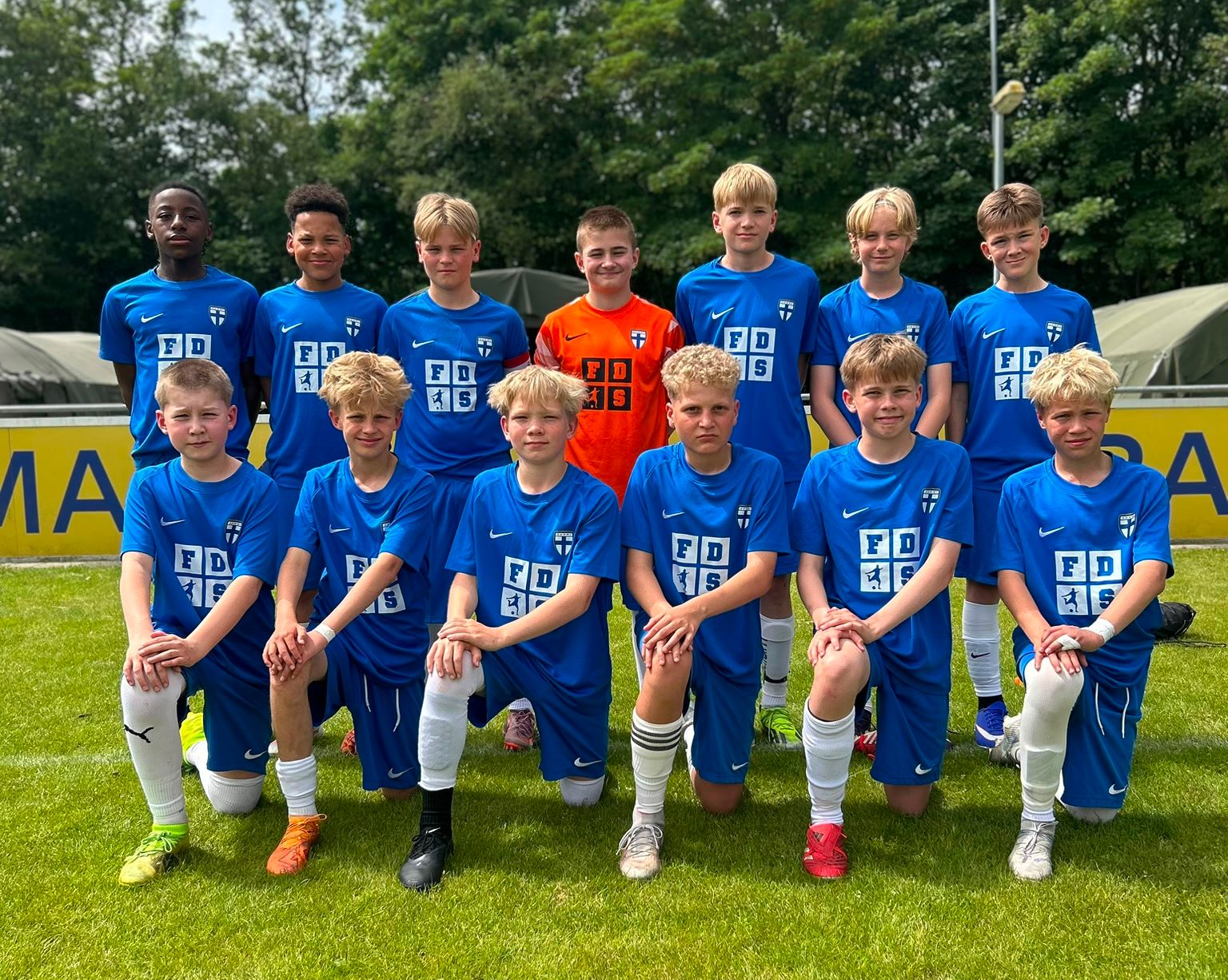 Finnish football team posing in blue jerseys on a grassy field, with one player in orange goalkeeper kit.