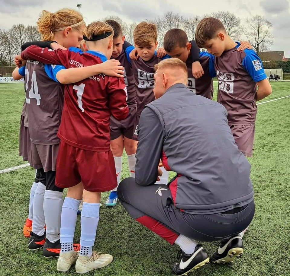 Football coach kneeling with youth players in a team huddle on a football field