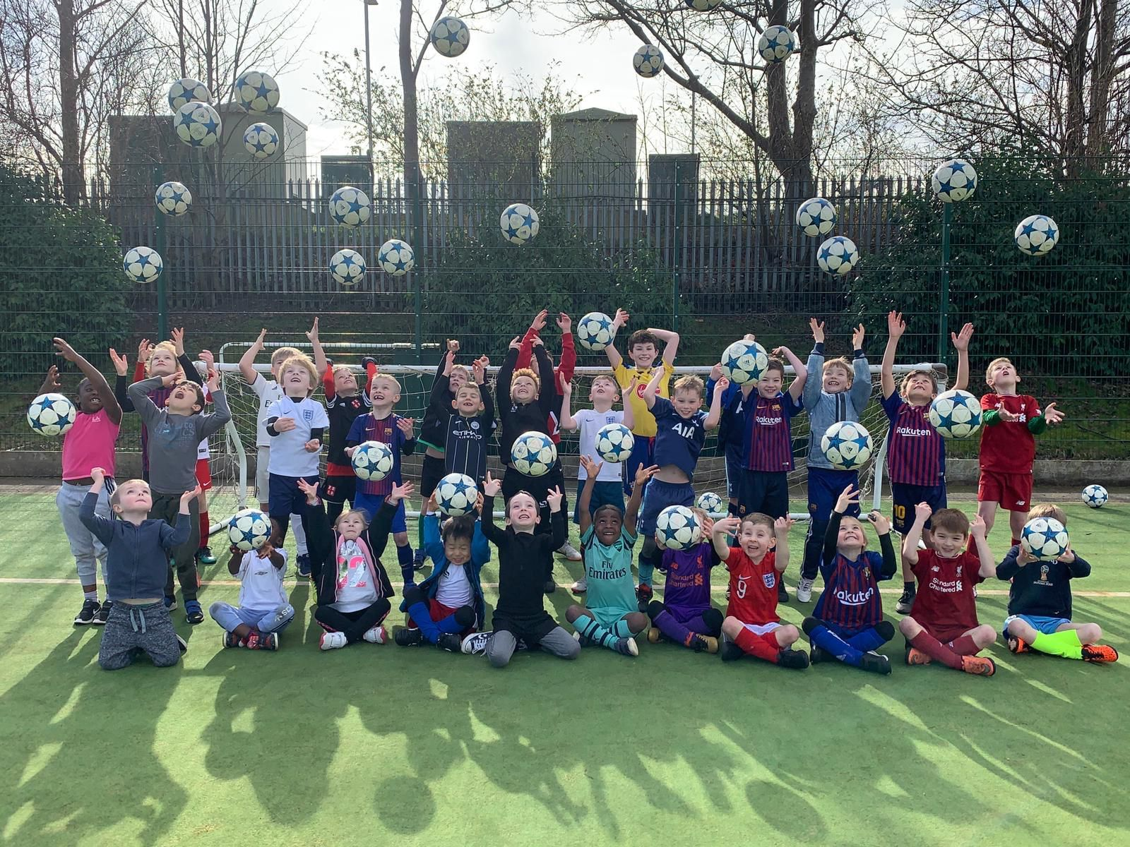 Group of children posing on a football field, throwing footballs in the air.