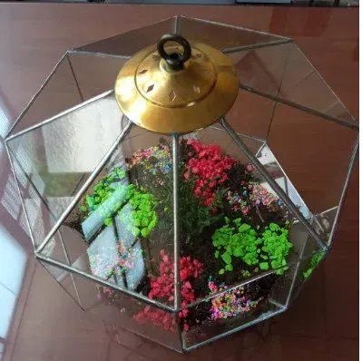 Colocación manual de una pieza de vidrio en un colorido mosaico de vidrieras sobre una mesa de trabajo.