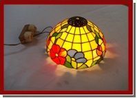 Panel floral de vidrieras con flores rojas, amarillas y azules en un marco de madera sobre una mesa en un estudio.