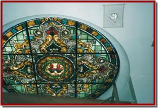 Vitral con una figura vestida con una túnica en el centro, ubicado en el interior de una iglesia.