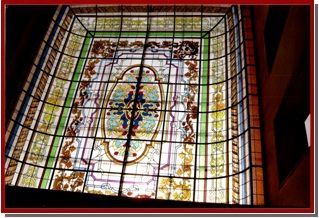 Panel floral de vidrieras con flores rojas, amarillas y azules en un marco de madera sobre una mesa en un estudio.