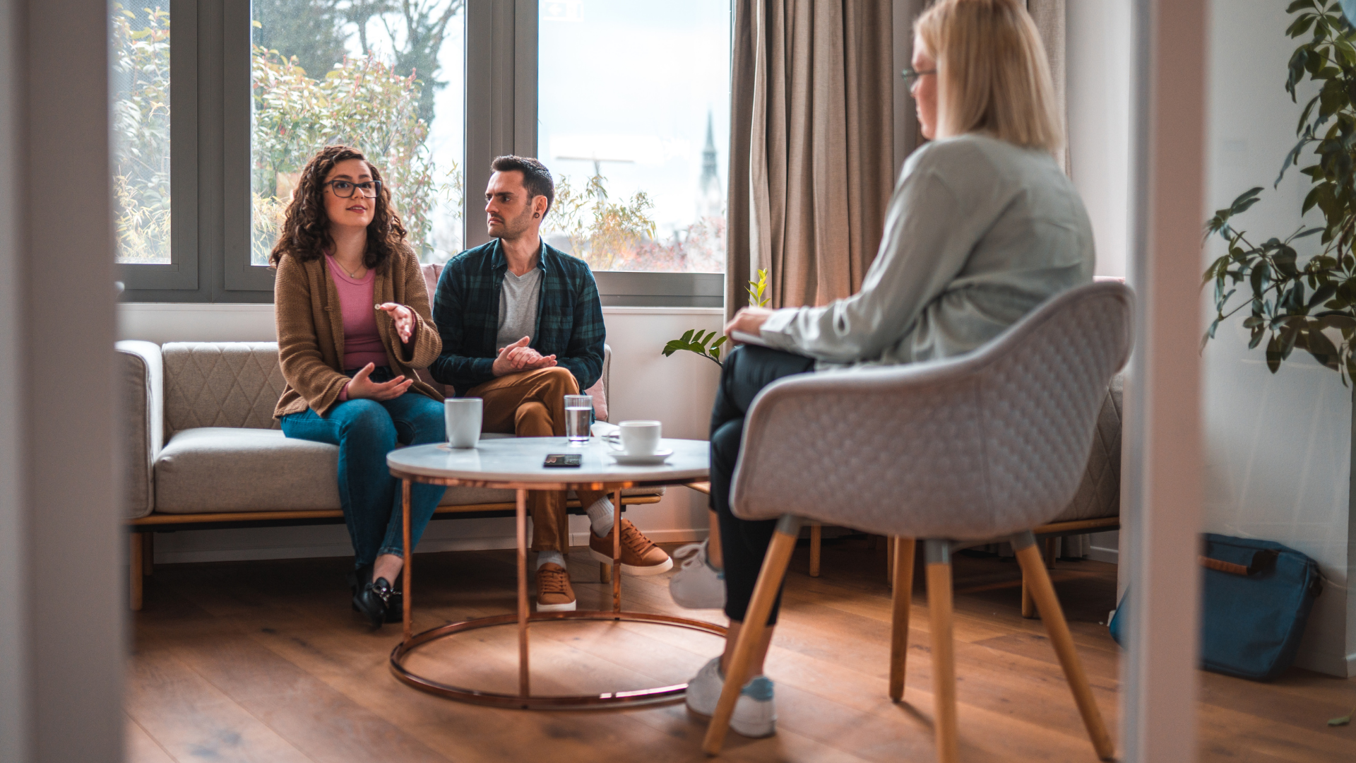 Couple in therapy session with a therapist in a bright room, talking.