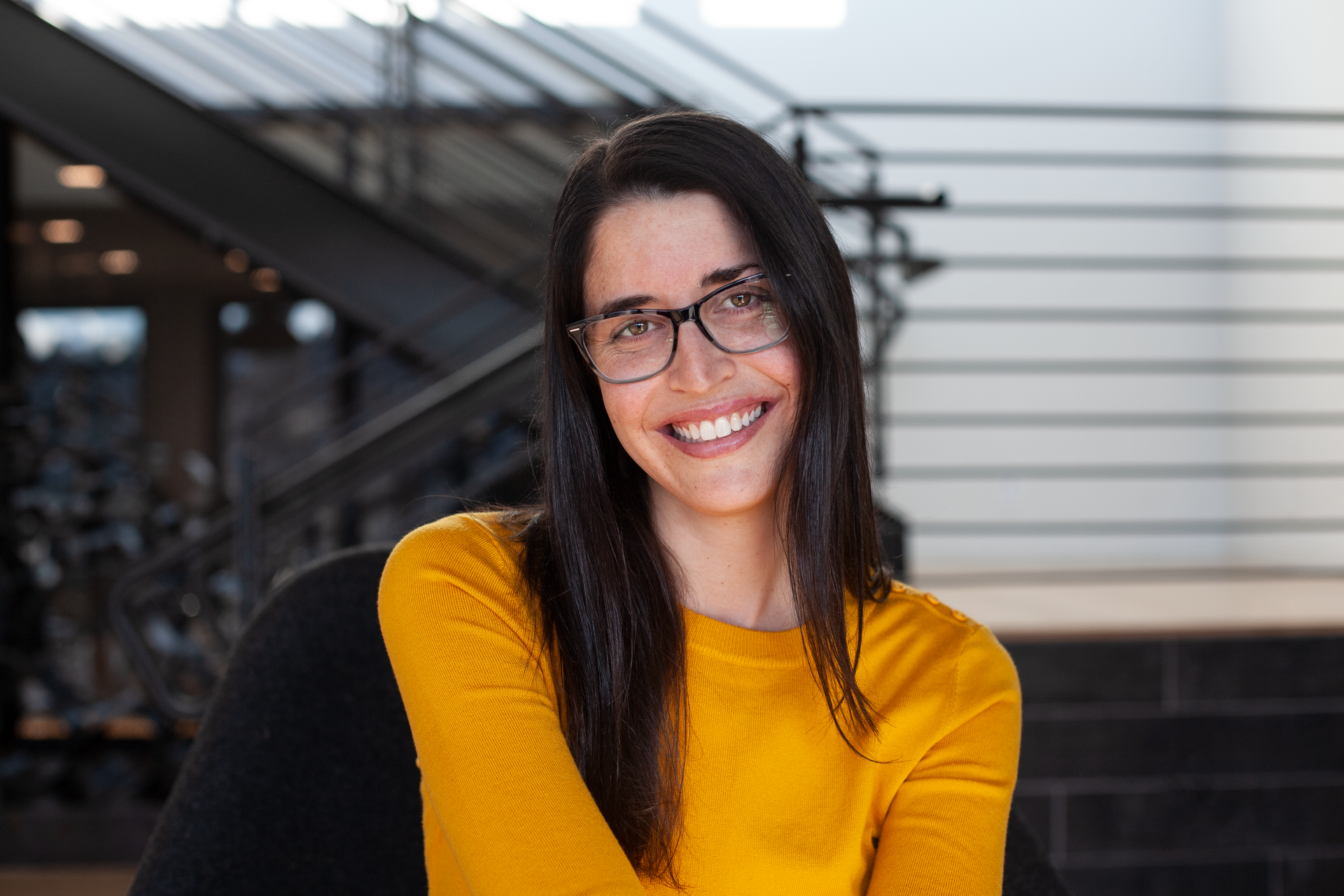Woman with glasses smiles while reading a book. Blue background.