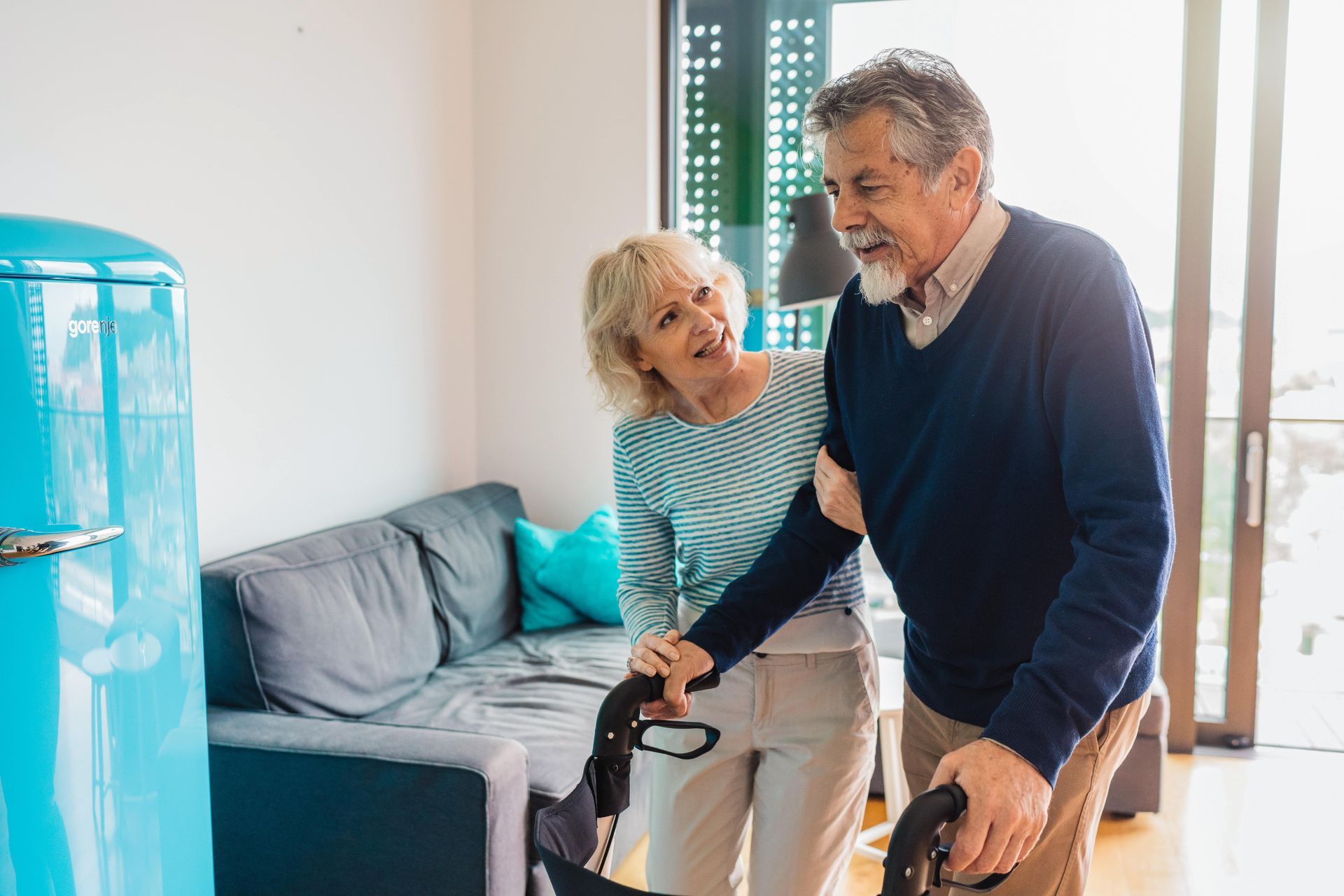 Older woman smiles as a caregiver places a hand on her shoulder indoors.