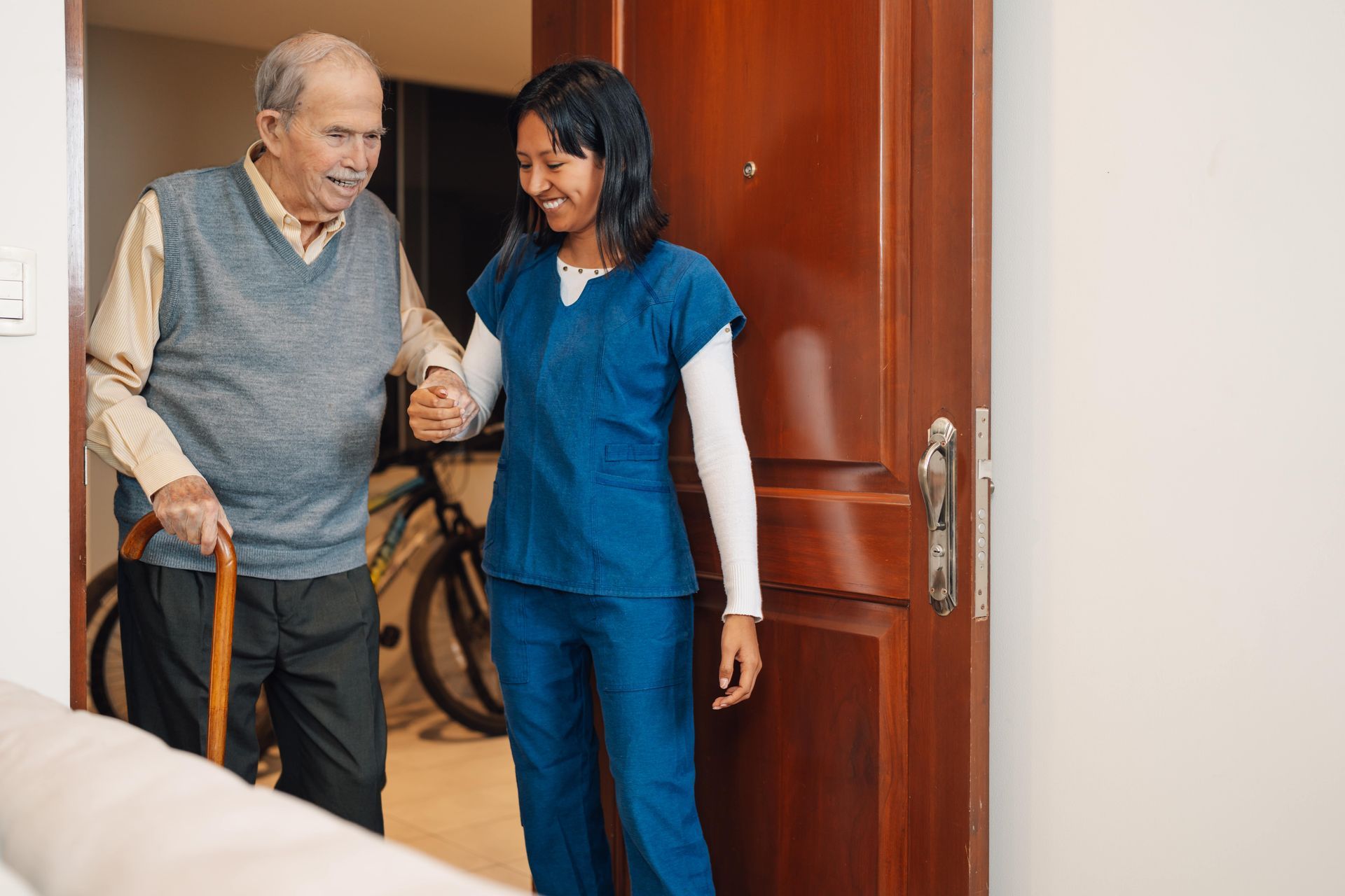 Two smiling nurses pose with a woman in a wheelchair, all inside a building, giving peace signs.