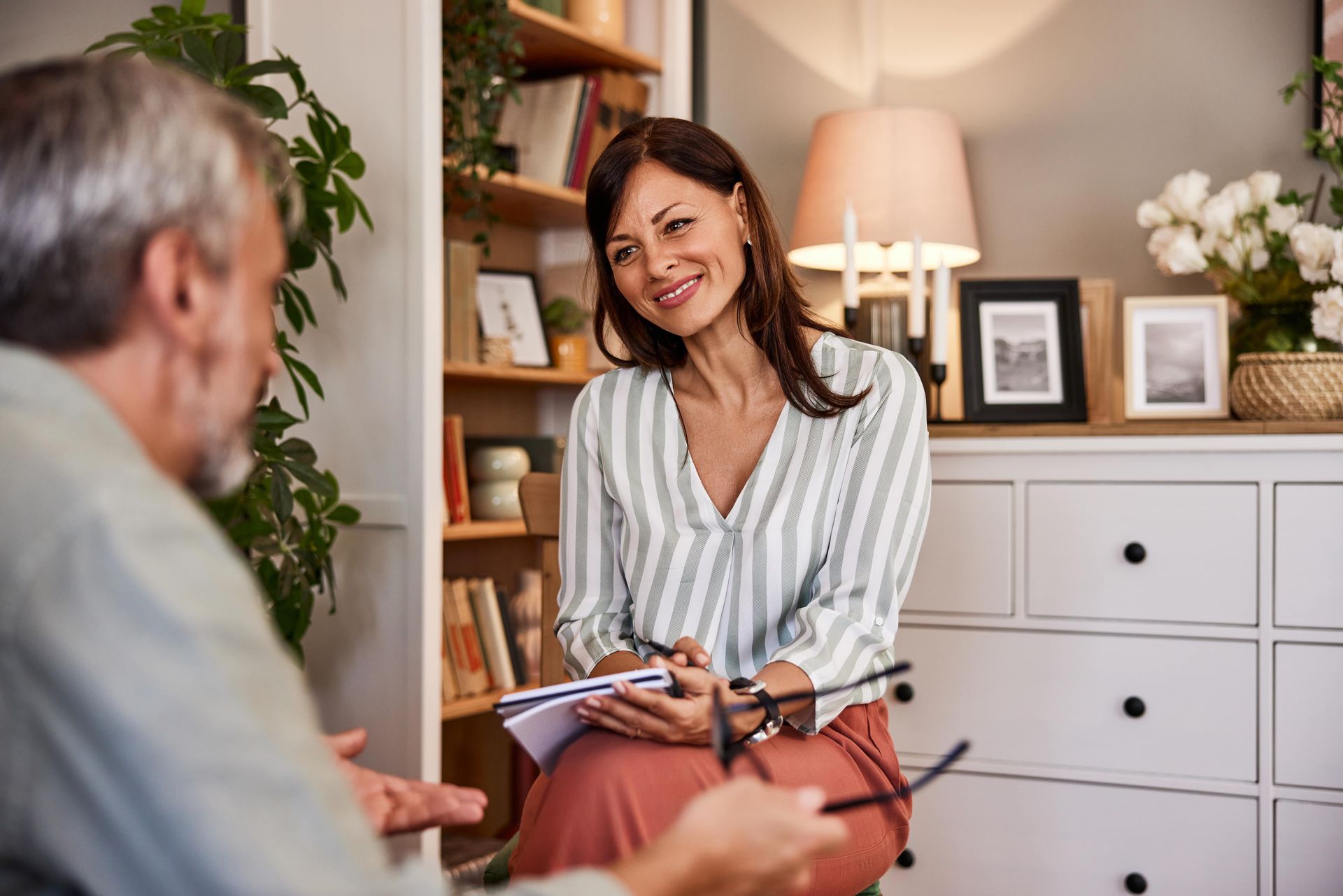 A person sits on a couch as another person takes notes on a clipboard.