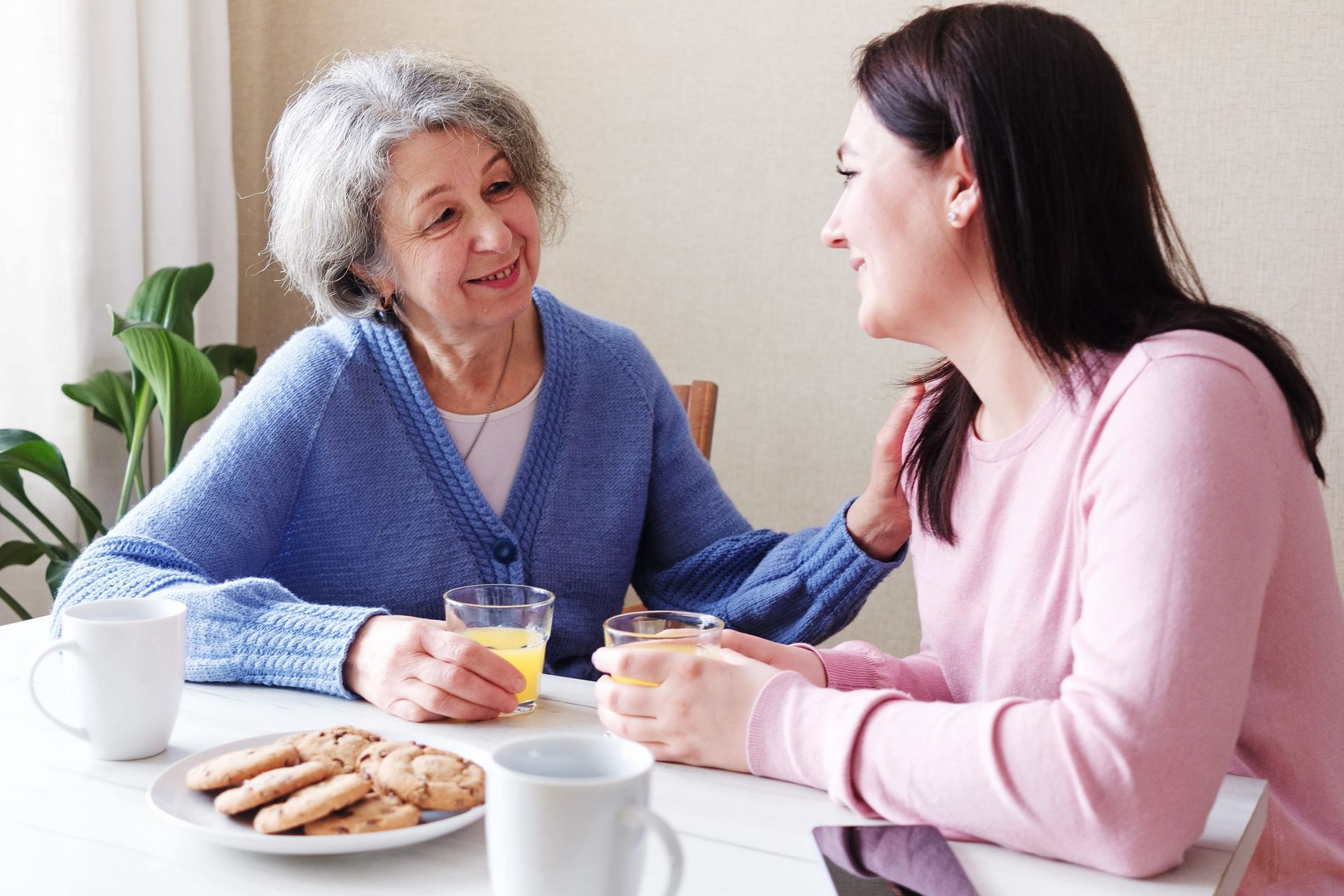 Adult daughter sitting with elderly mother at kitchen table.
