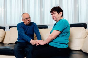 Person holding the hands of an older person. Purple sweater, light skin, supportive gesture.