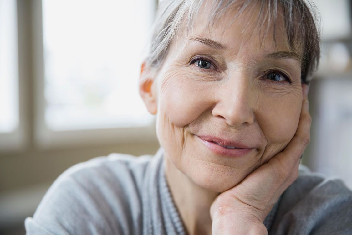 Woman with glasses smiles while reading a book. Blue background.