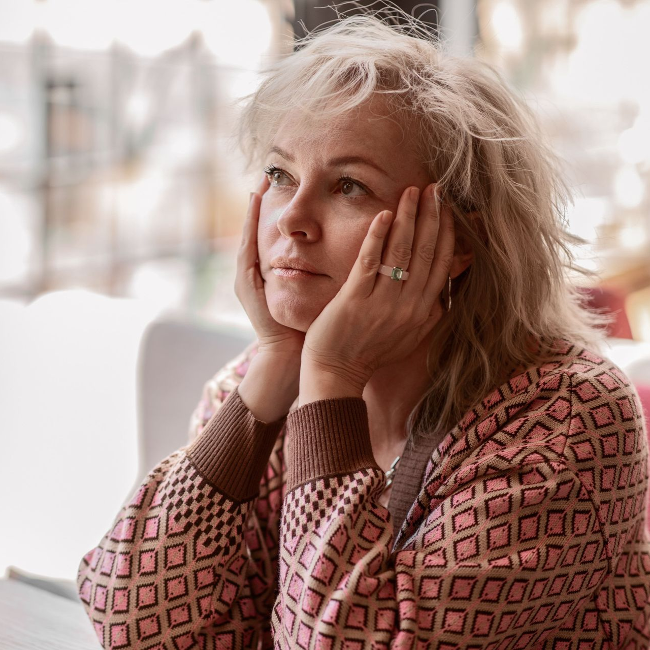 Woman stressed at desk, surrounded by hands holding phone, papers, and watch.