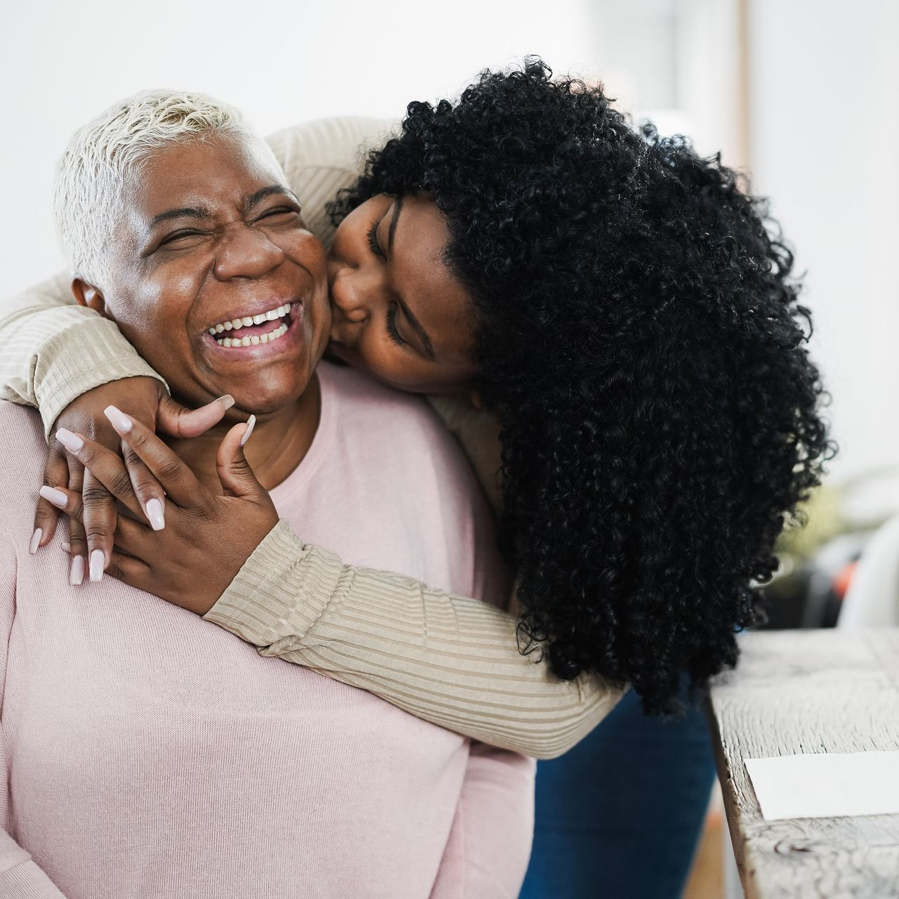 Woman with glasses smiles, reading a book on a couch, red wall behind her.