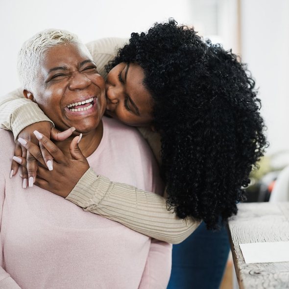 Woman with glasses smiles, reading a book on a couch, red wall behind her.