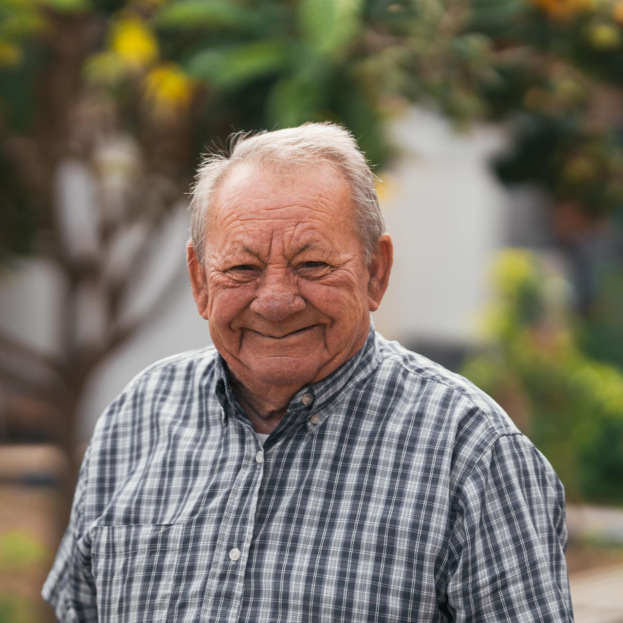 Woman with glasses smiles at camera while working on laptop. Blue sweater, modern setting.