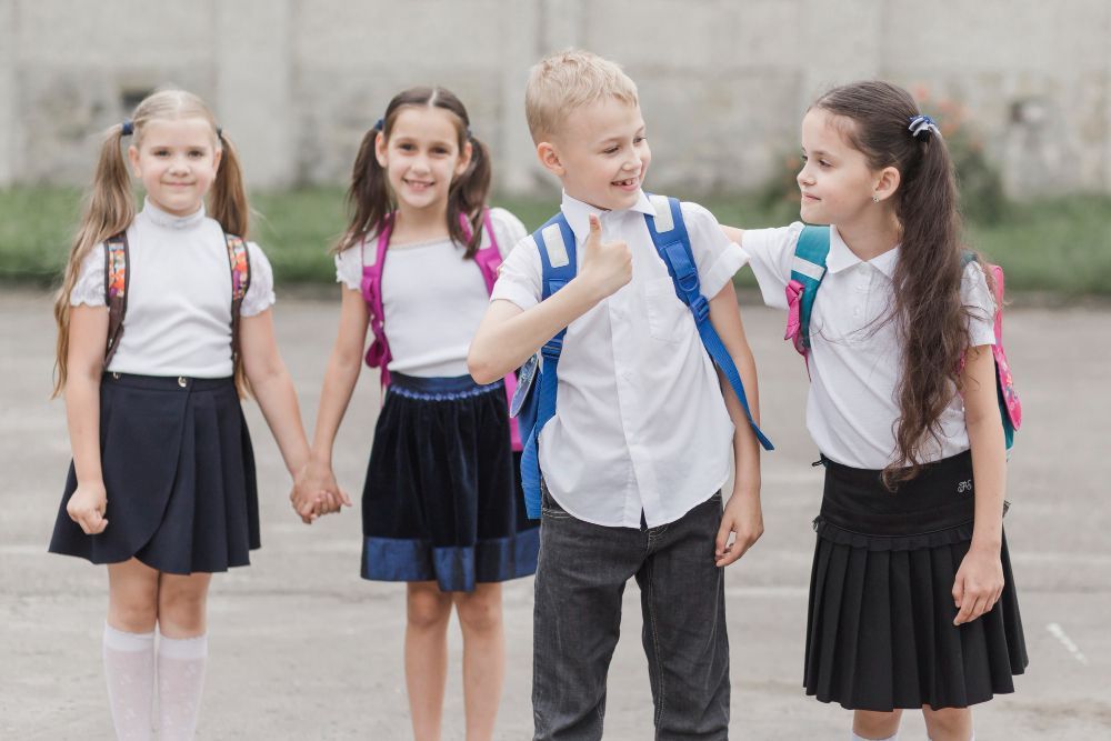 A group of children in school uniforms are holding hands and giving each other a thumbs up.