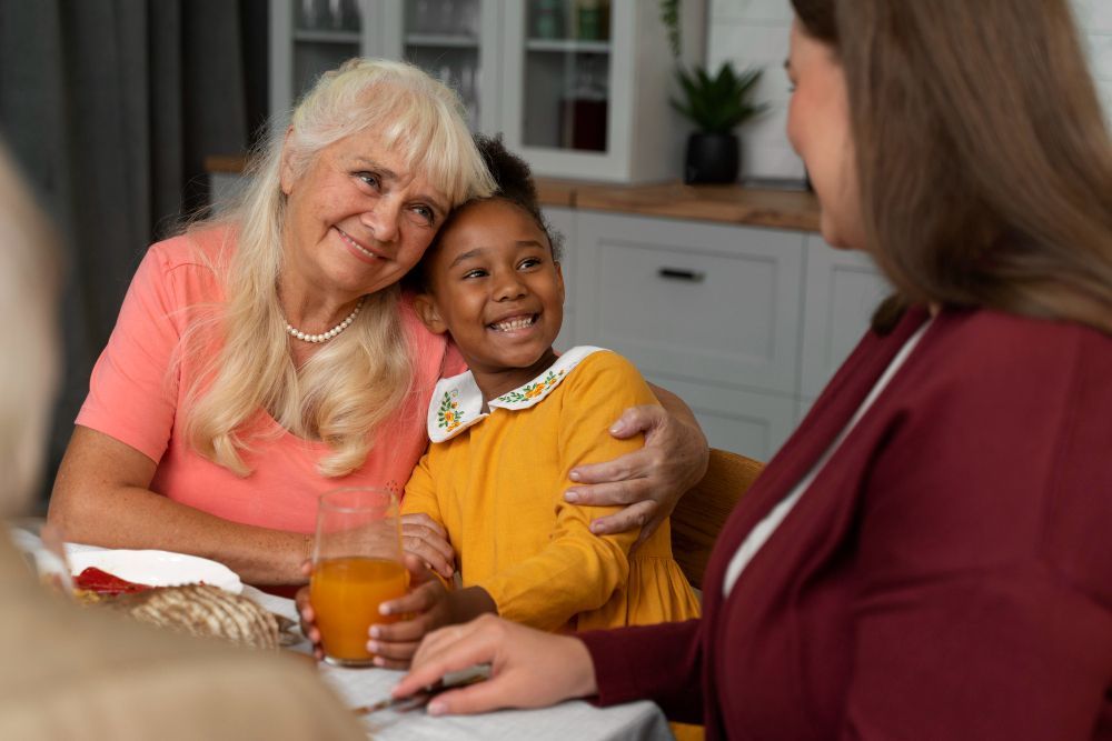 A woman is sitting at a table with two older women and a little girl.