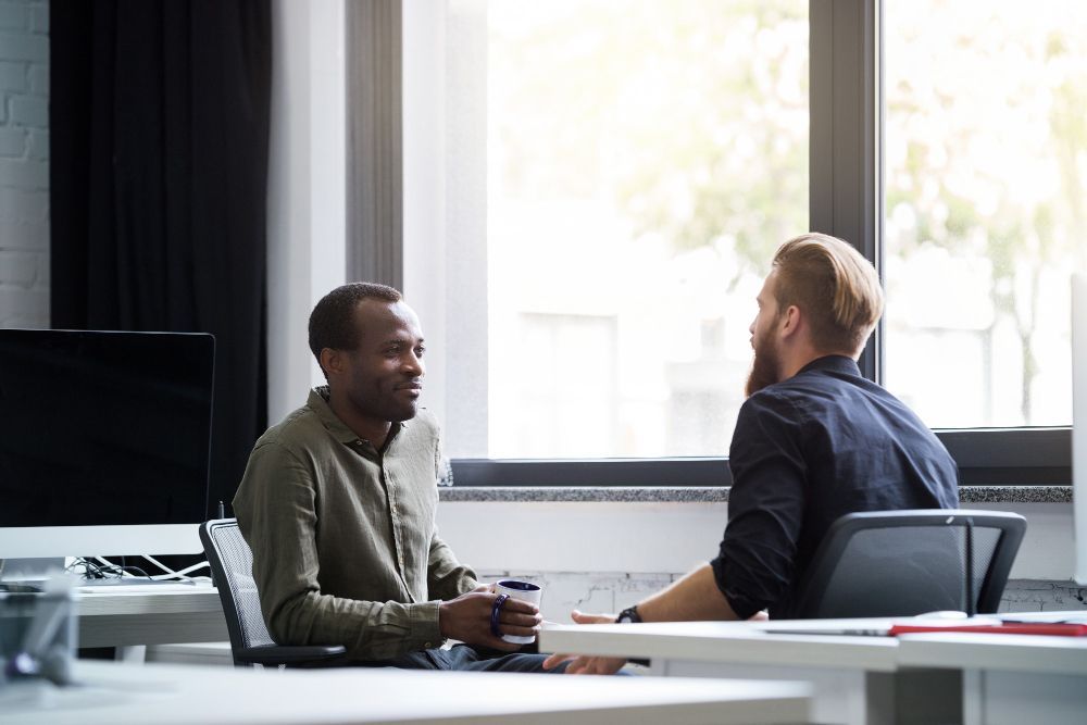 Two men are sitting at a table having a conversation in an office.