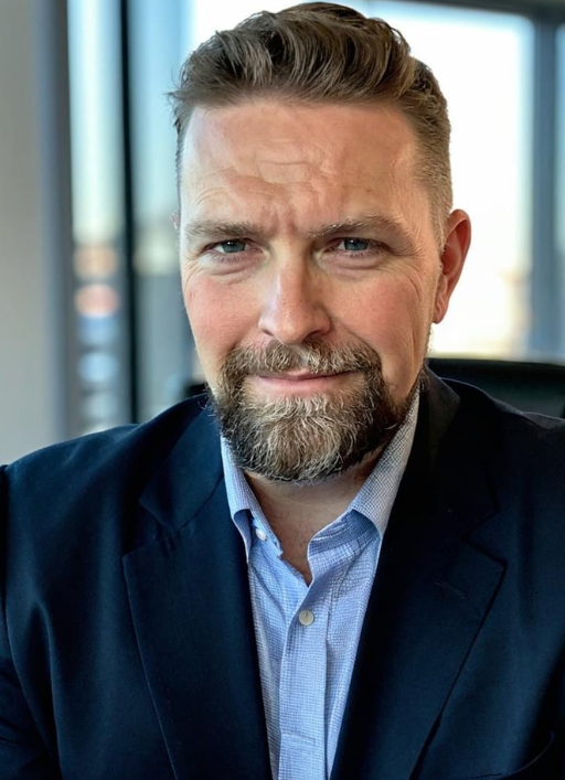 A man with a beard is wearing a suit and looking at the camera.