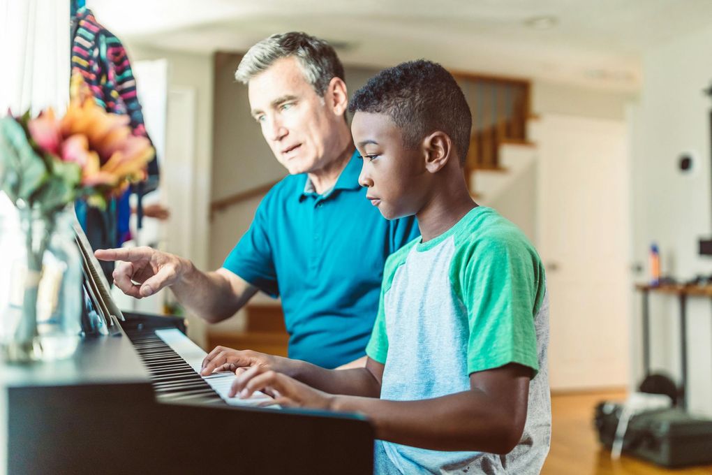 A man is teaching a young boy how to play the piano.