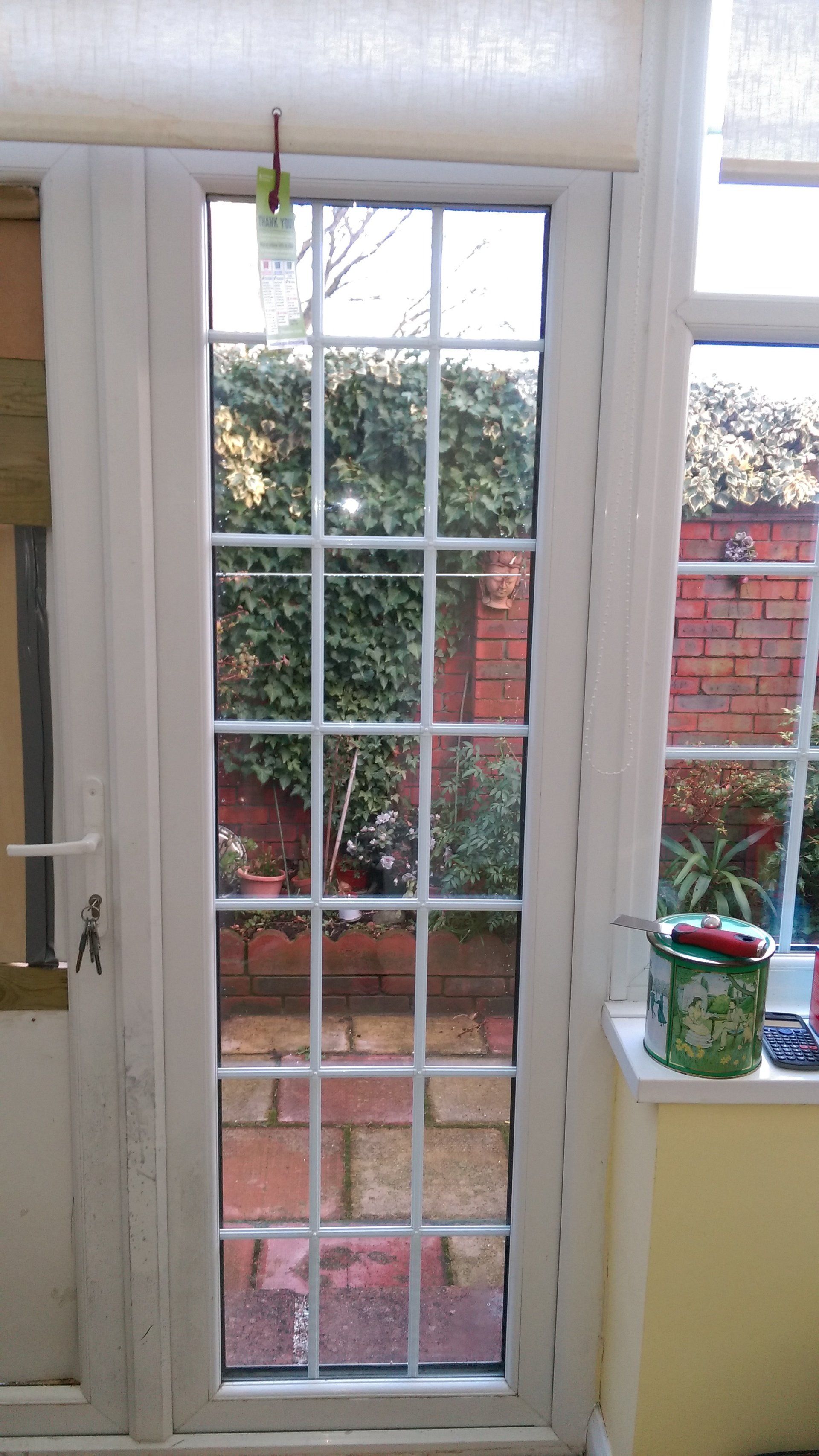 A white door with a brick wall behind it and a potted plant on a window sill.