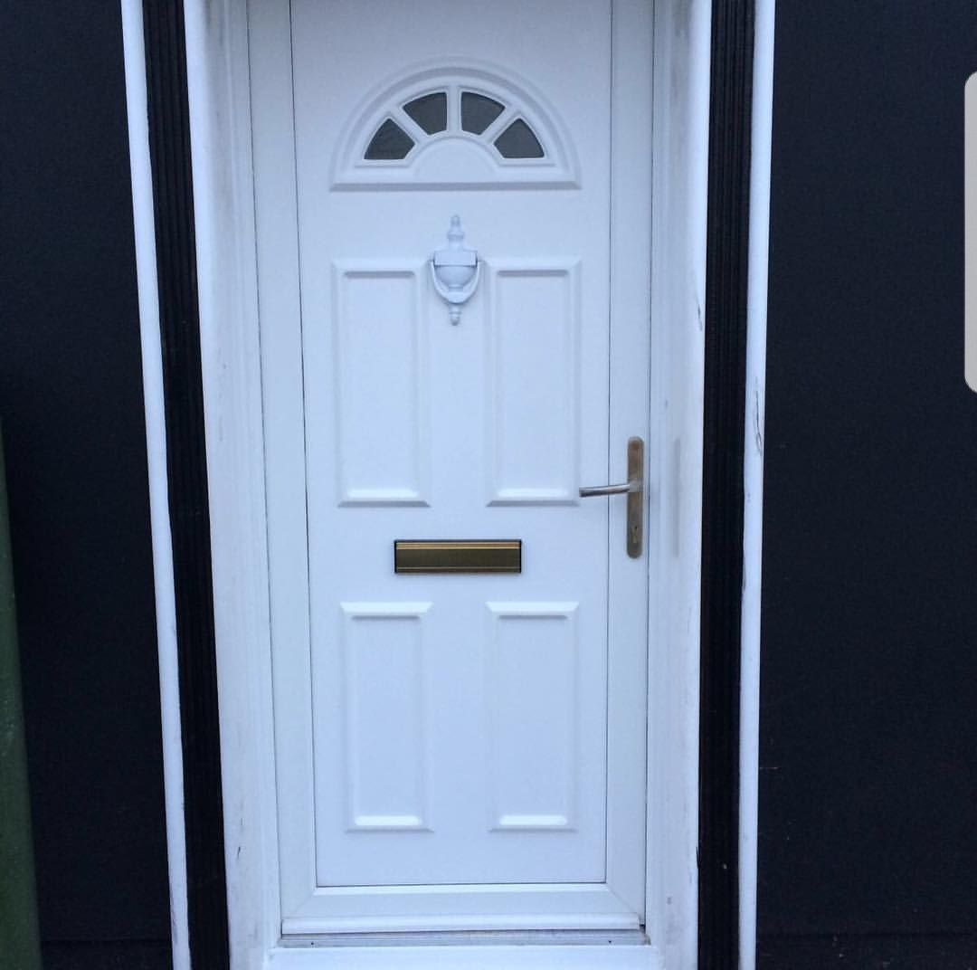 A white door with a window on it is on a black wall.