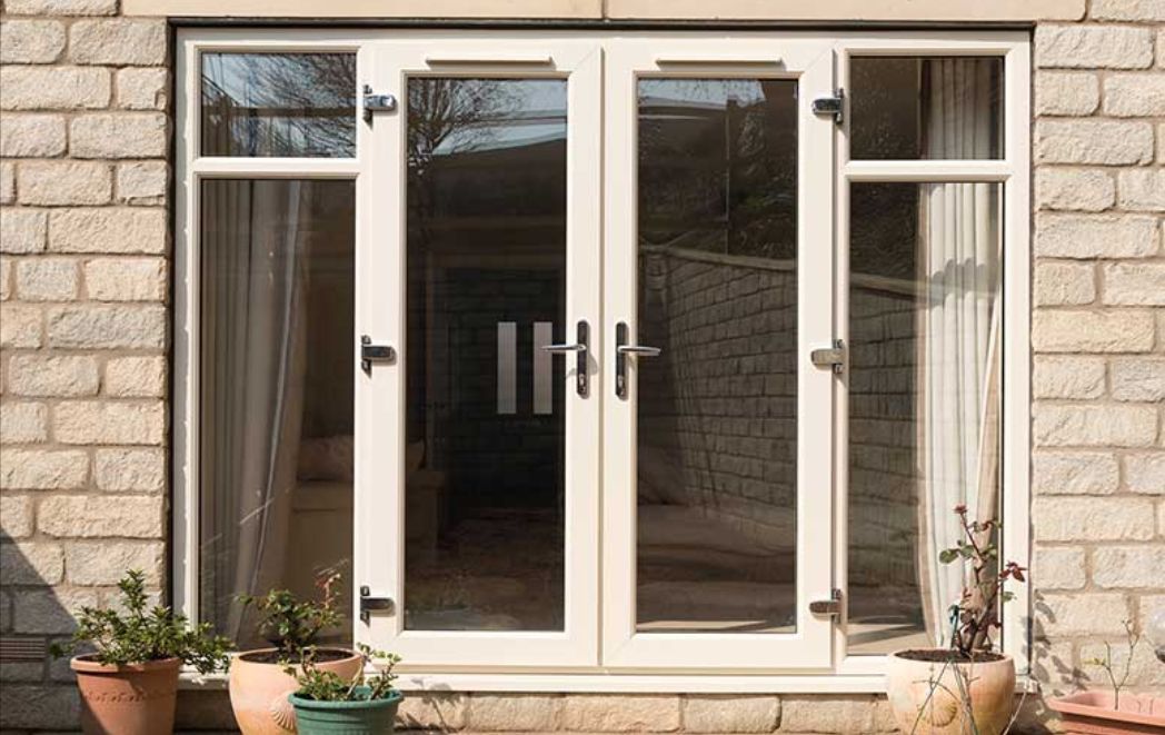 A white french door is sitting on a brick wall next to potted plants.