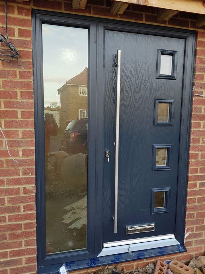 A black door with a stainless steel handle is on a brick wall.