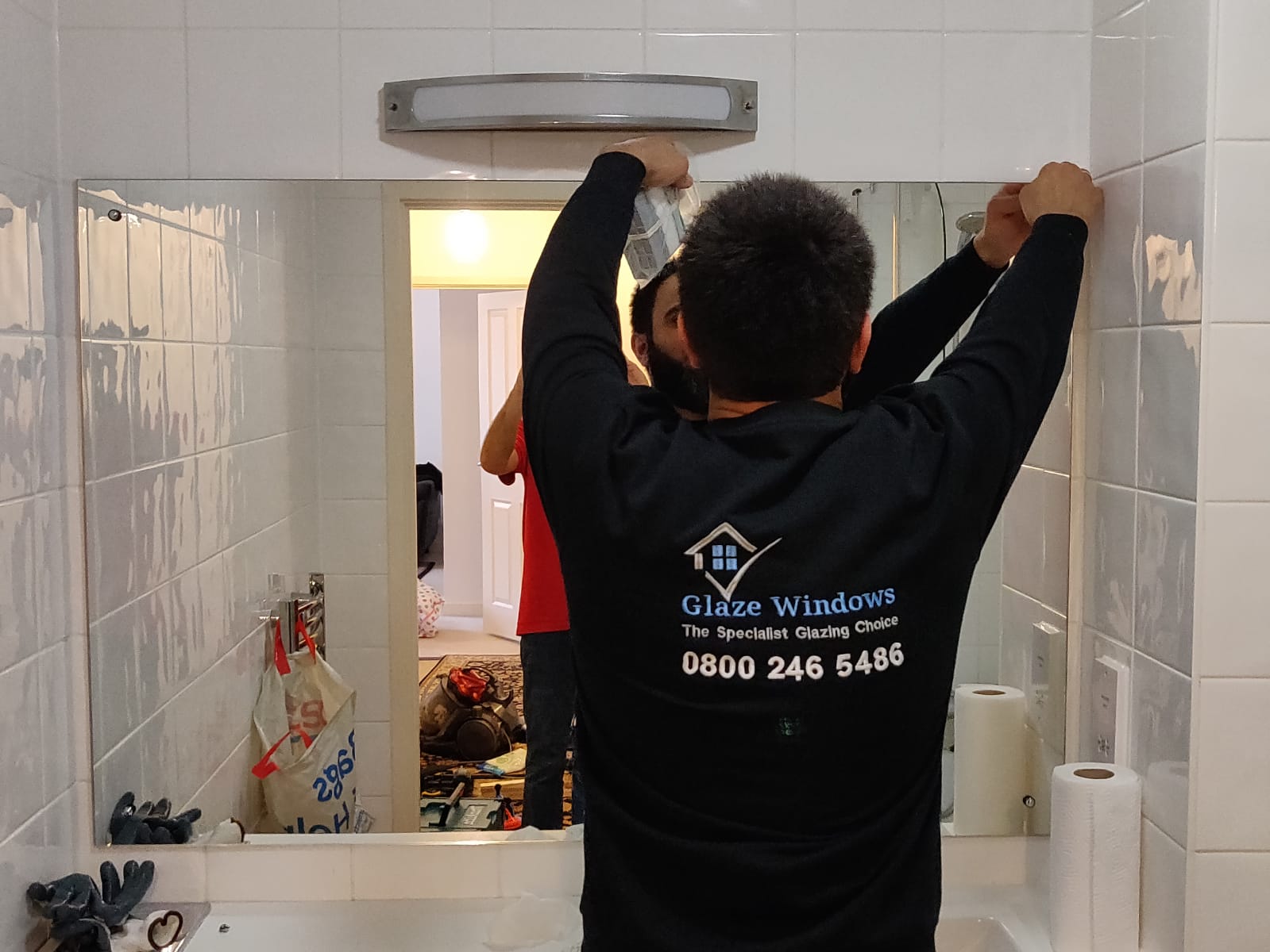 A man is installing a mirror in a bathroom.