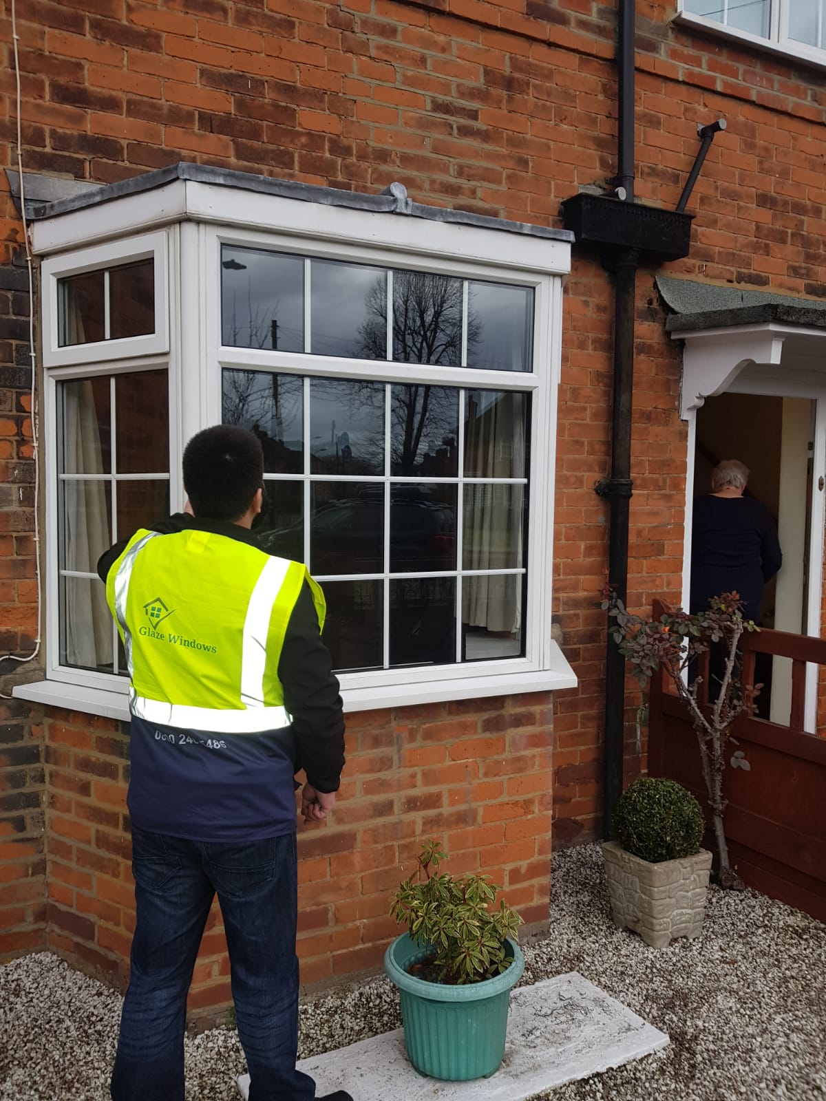 A man in a yellow vest is standing in front of a window