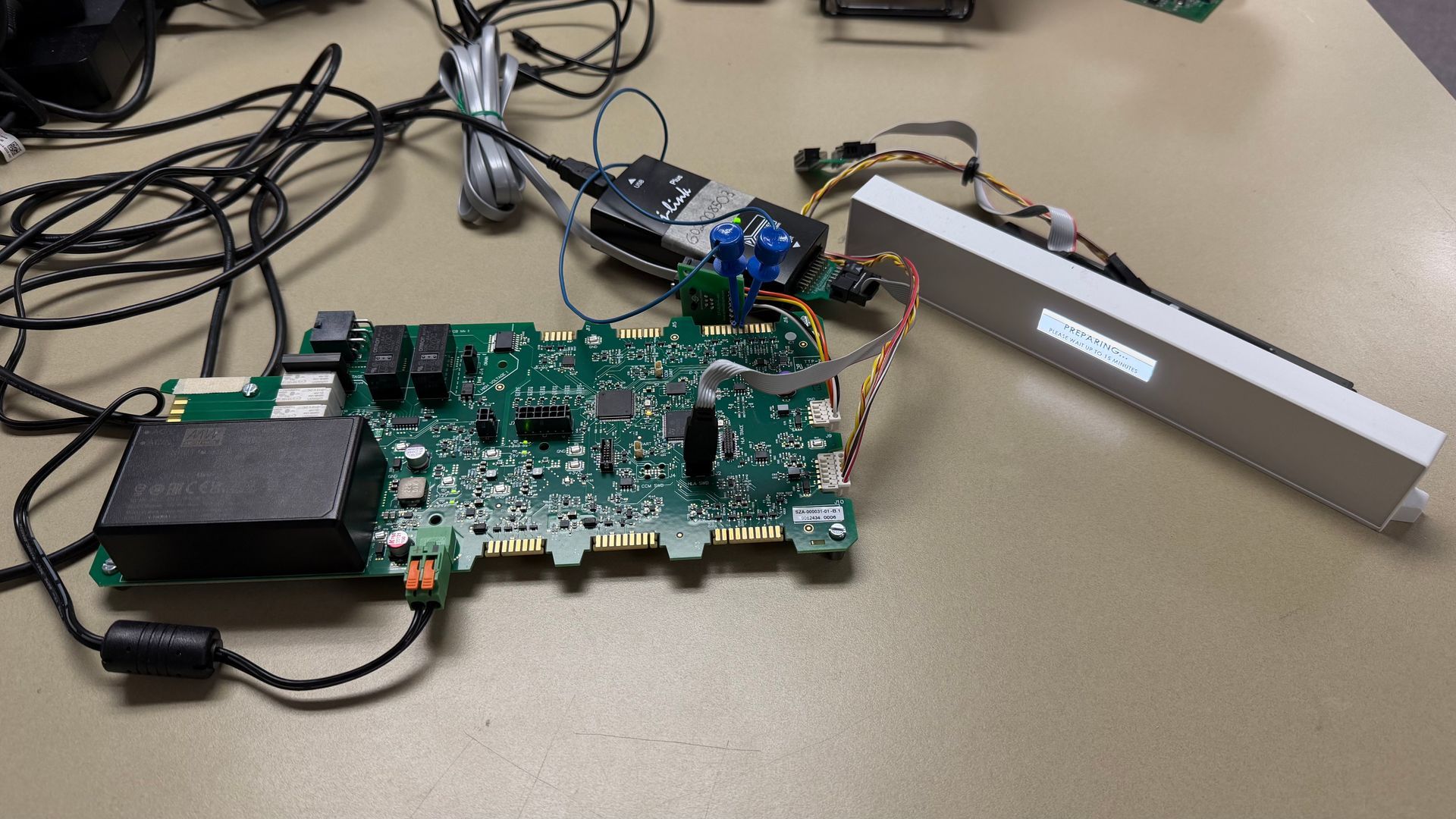A green circuit board connected to a white electronic display module and power cables on a beige table.
