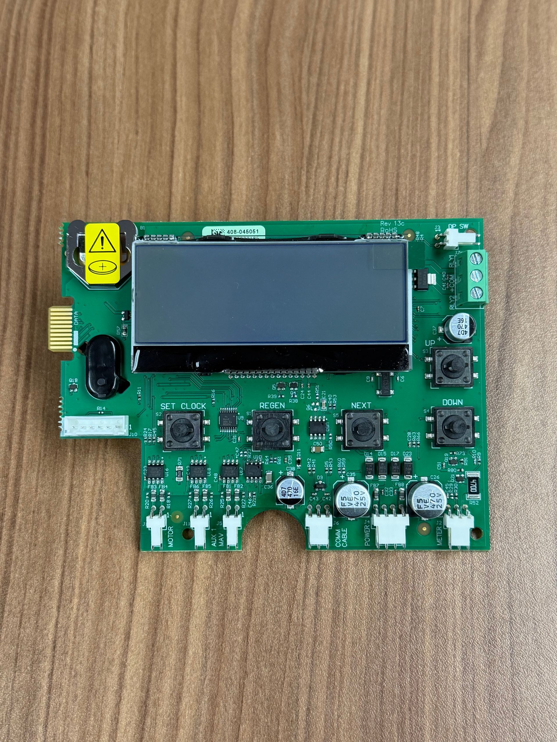 A green electronic circuit board with a central rectangular display, several small push buttons, and bottom connectors.