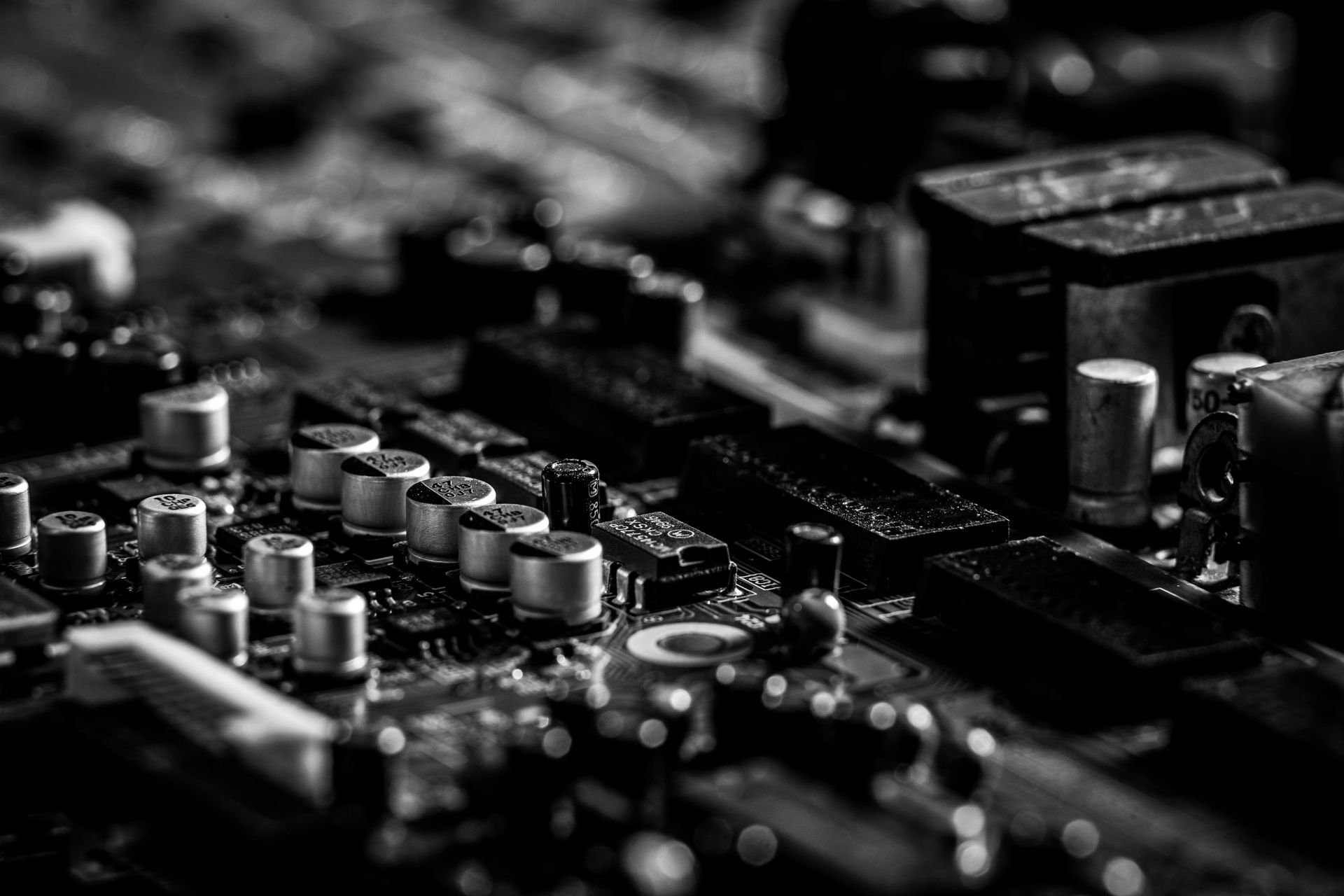 A close-up, high-contrast monochrome view of an electronic circuit board with various capacitors and components.